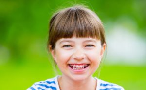 Happy young girl with pink braces smiling outdoors with a bright background in Mansfield