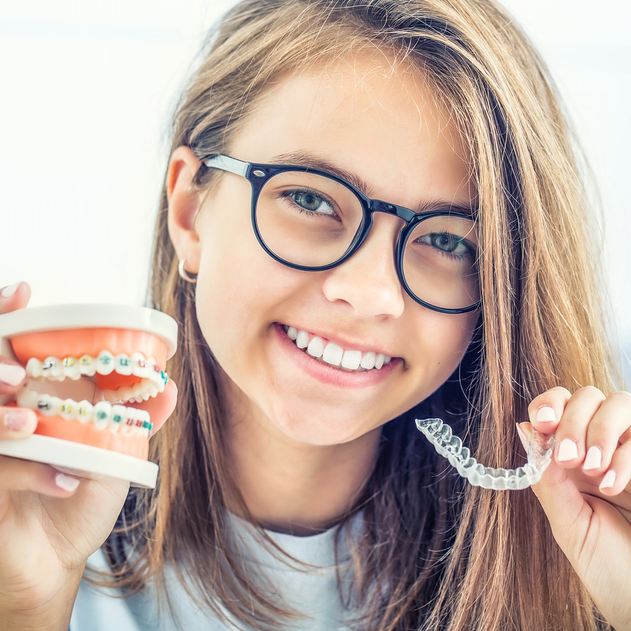 Girl holding models of Invisalign and traditional braces in Mansfield, TX