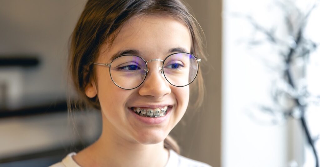 Young girl with braces and glasses smiling after early orthodontic care in Mansfield, TX