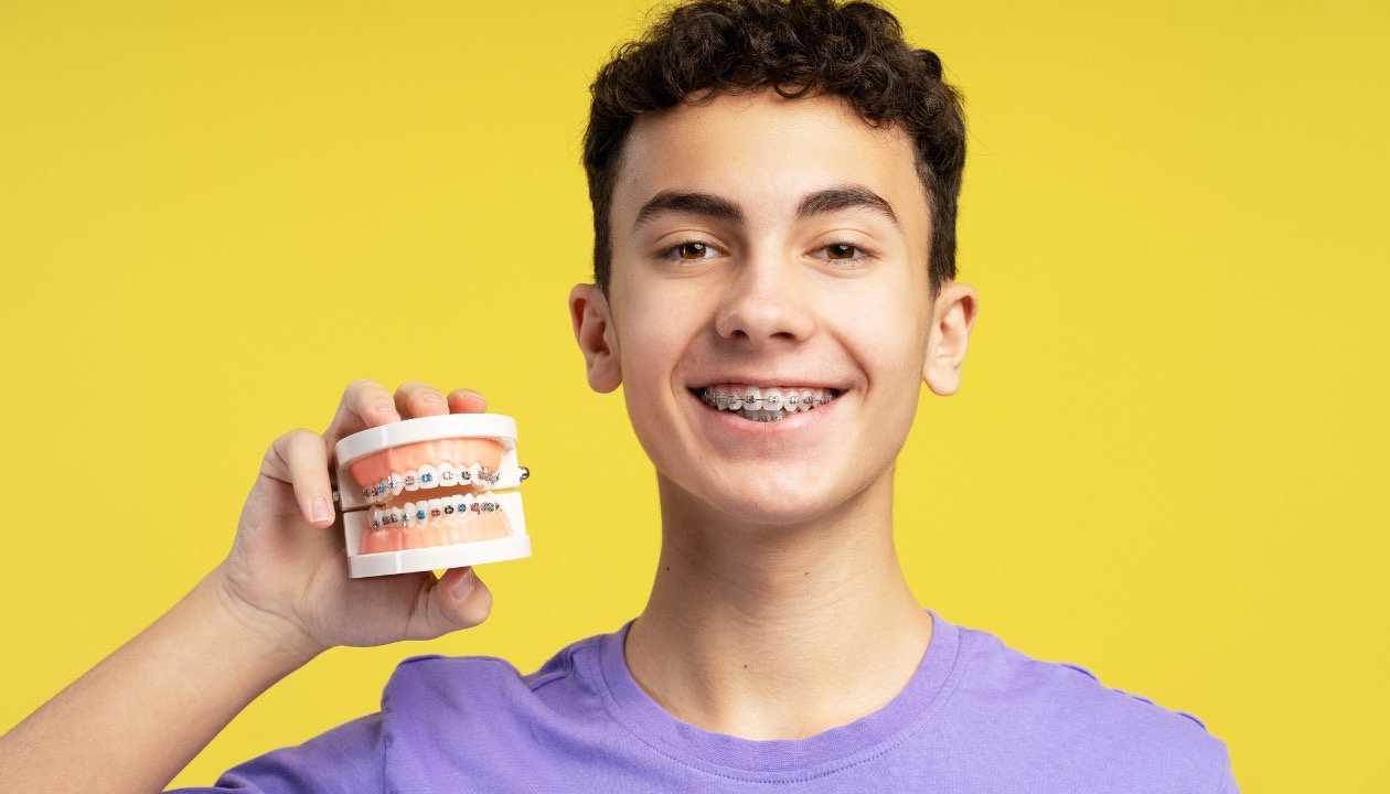 Teen boy smiling with braces holding dental model in Mansfield, TX