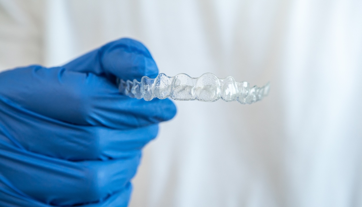 Close-up of hand in blue glove holding clear Invisalign aligner for teen orthodontic treatment